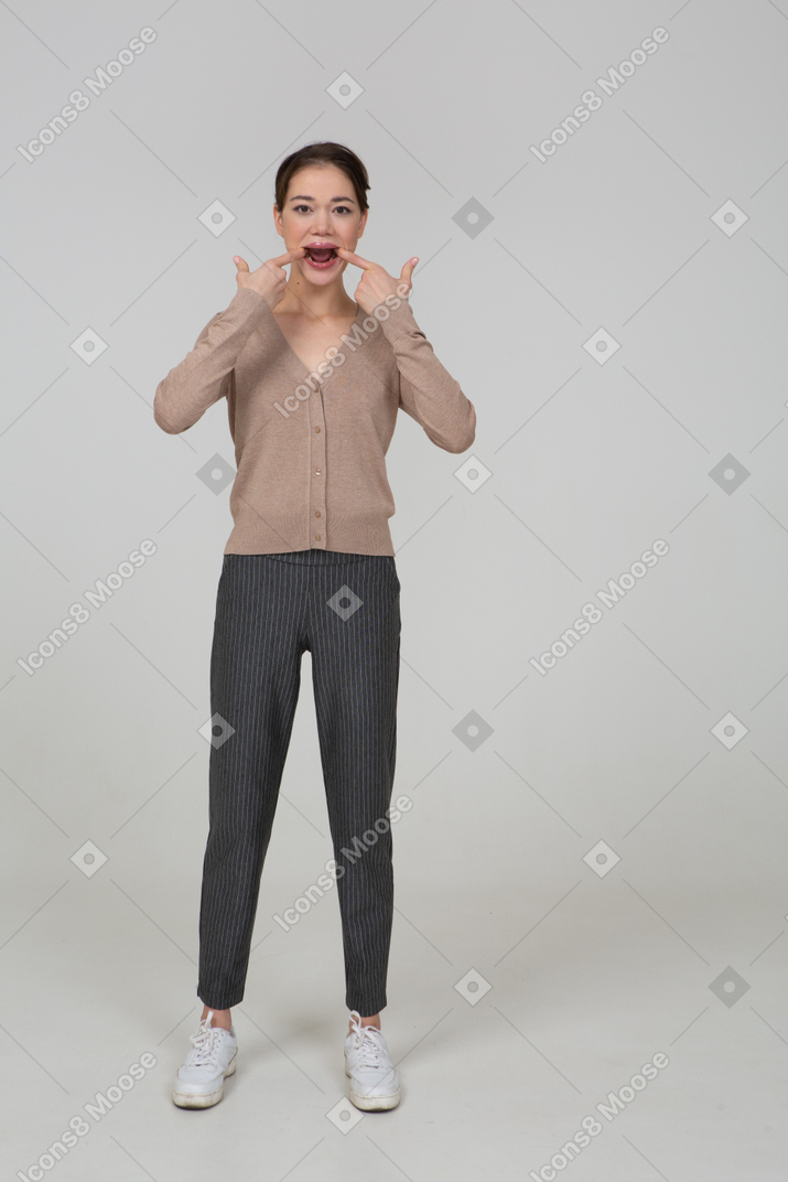 Front view of a young lady in pullover and pants touching her mouth