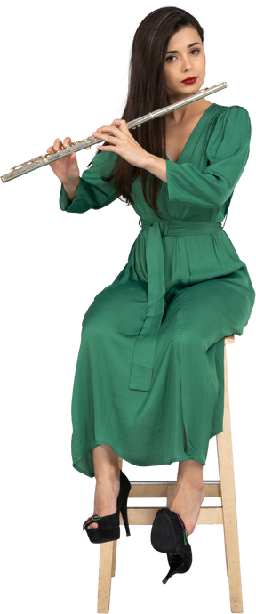 一位年轻的女士穿着绿色的衣服，坐在椅子上，同时演奏单簧管的前视图
