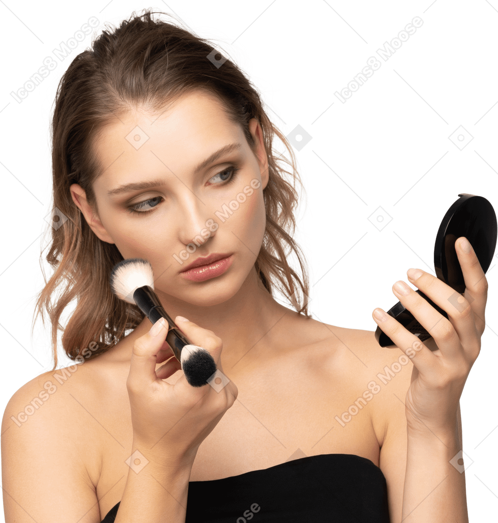 Vista frontal de una mujer joven que aplica polvos faciales mientras sostiene un espejo