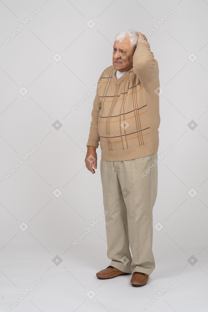 Front view of an old man in casual clothes standing with hand on head