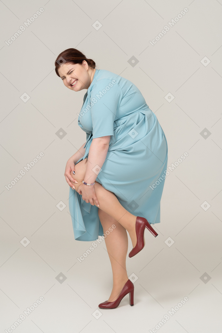 Side view of a woman in blue dress touching her injured knee