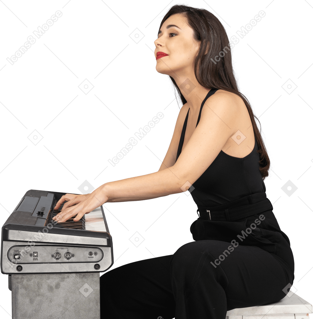Vue latérale d'une jeune femme souriante en costume noir assis et jouant du piano