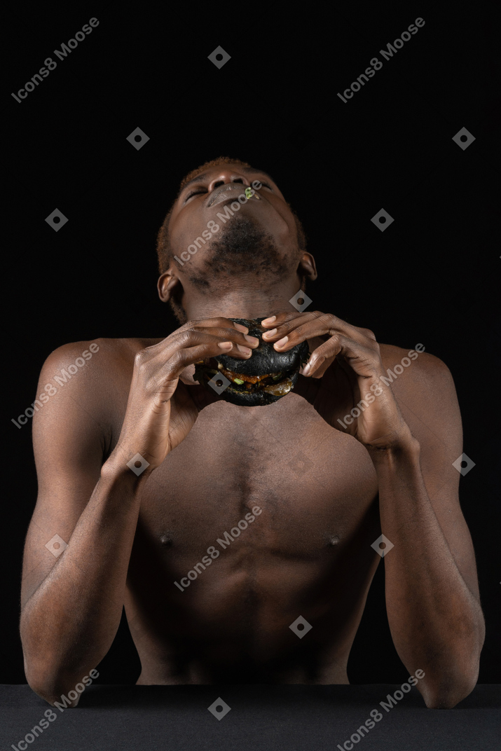 Vista frontal de un joven afro disfrutando de una hamburguesa