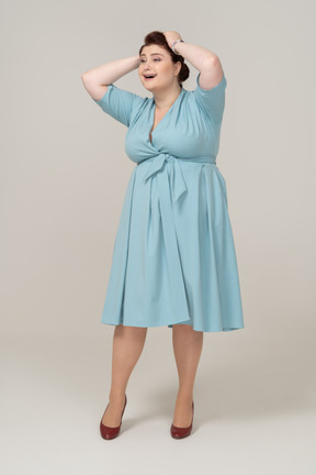 Вид спереди женщины в синем платье позирует с руками на голове