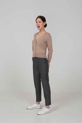 Vista di tre quarti di una giovane donna in pullover e pantaloni che mostra la lingua