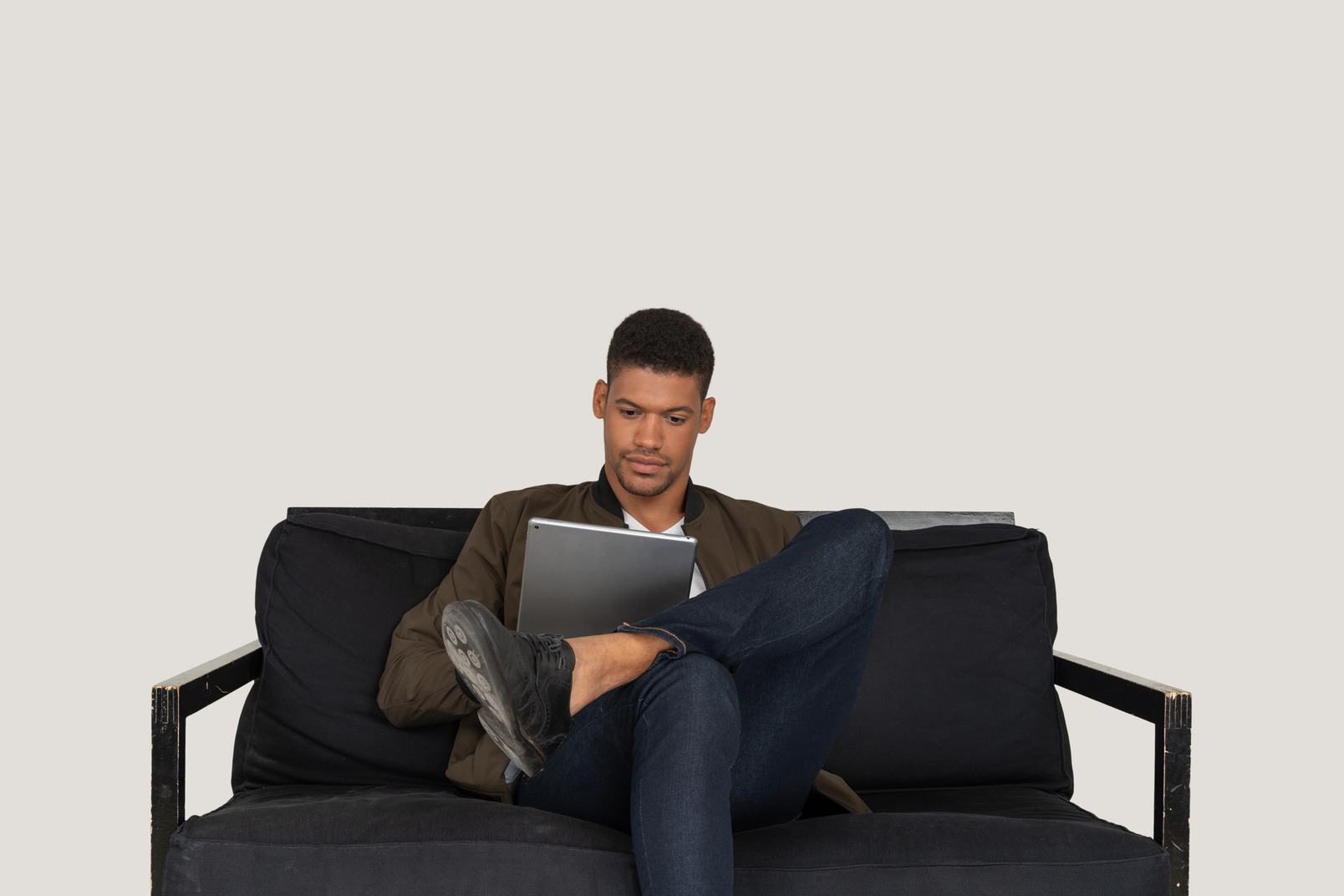タブレットを保持しながらソファに座っている若い男の正面図 のフォト