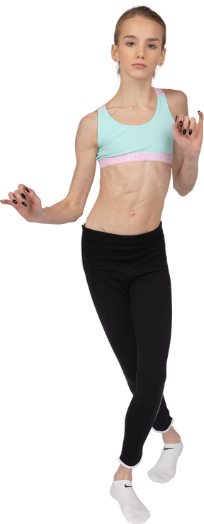 Vista frontal de una jovencita en ropa deportiva cruzando las piernas y gesticulando mientras baila