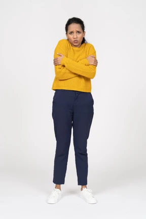 Front view of a cute girl in casual clothes hugging herself and looking at camera