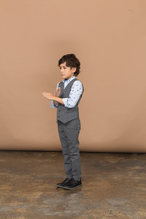 Vista lateral de um menino de terno cinza mostrando o gesto de parada