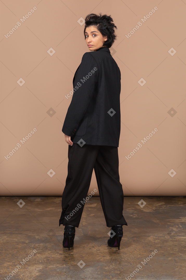 Vista traseira de uma empresária de terno preto e olhando para a câmera