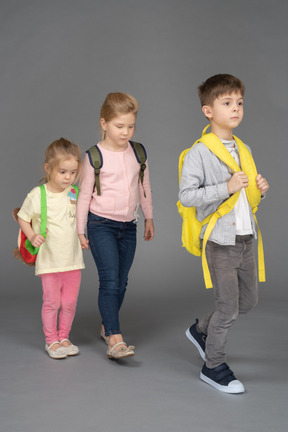 Трое детей с рюкзаками возвращаются в школу