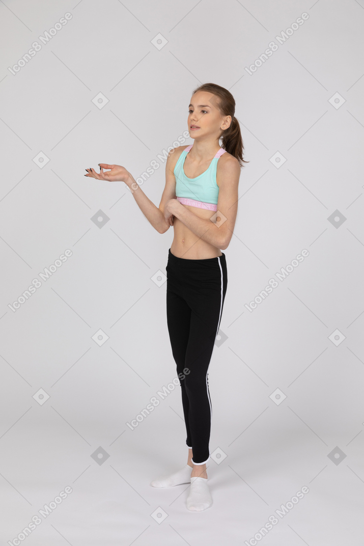 Вид в три четверти девушки-подростка в спортивной одежде, поднимающей руку и рассуждающей