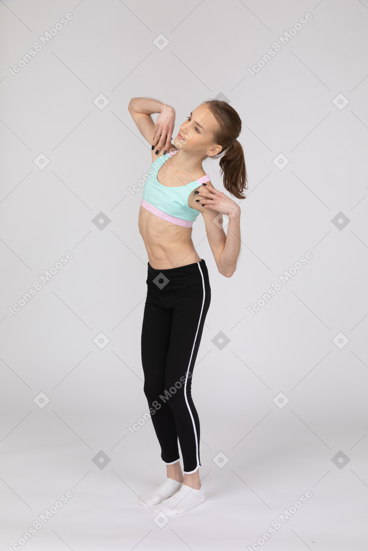 Three-quarter view of a teen girl in sportswear touching her shoulders and tilting right