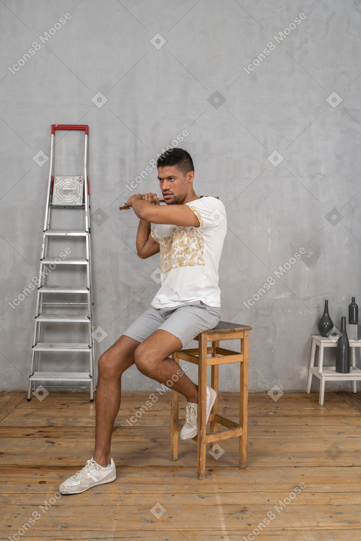Three-quarter view of a man on a stool swinging an ukulele and frowning