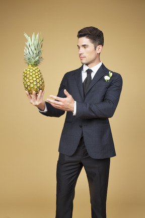 Groom in black suit holding a pineapple and like complimenting it