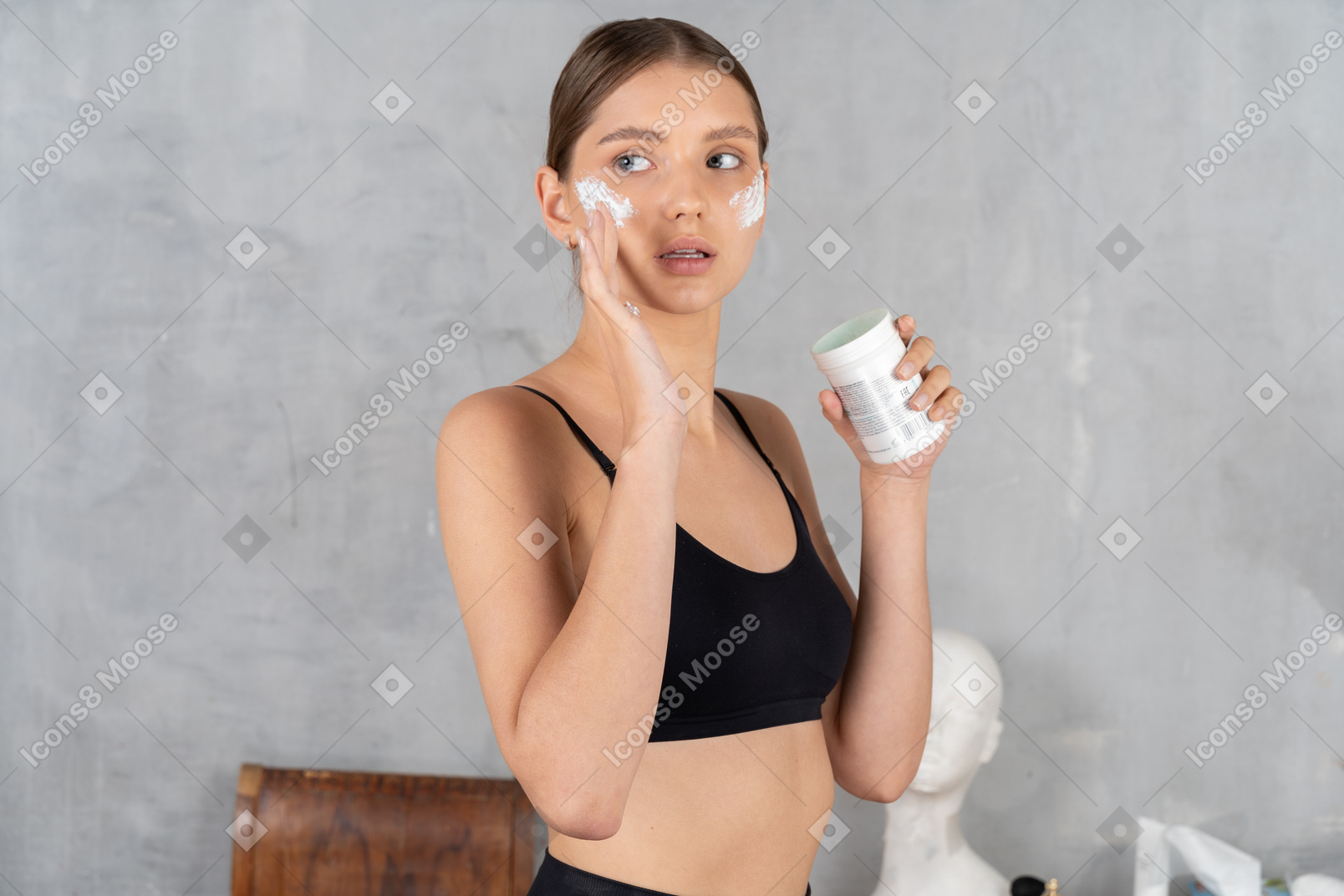Mujer joven mirando a un lado y aplicando crema en la cara