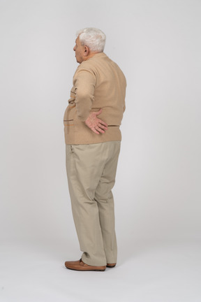 Side view of an old man in casual clothes suffering from back pain