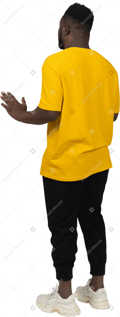 Vista posteriore di tre quarti di un giovane uomo dalla pelle scura in maglietta gialla che allunga le braccia