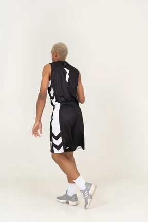 Vista posterior de tres cuartos de un confundido joven jugador de baloncesto haciendo una finta