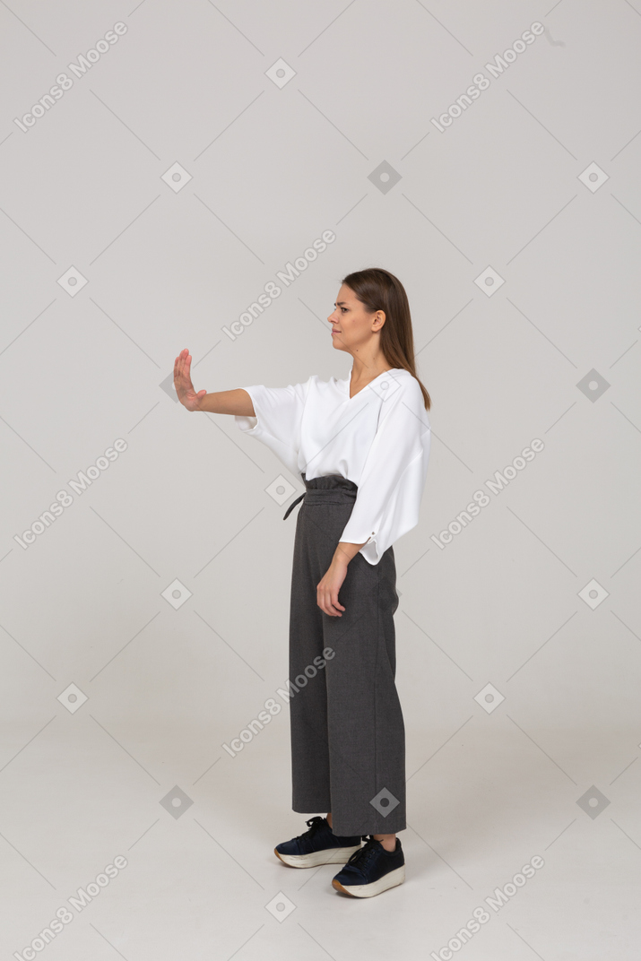 Трехчетвертный вид недовольной молодой леди в офисной одежде, протягивающей руку