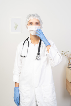 Vista frontal de uma jovem médica na máscara tocando o rosto