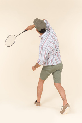 Giovane uomo caucasico tenendo la racchetta da tennis e in piedi di nuovo alla telecamera