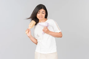 Joven mujer india peinarse con cepillo de pelo y secador de hierro