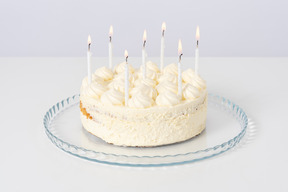 White cake with candles on a glass plate