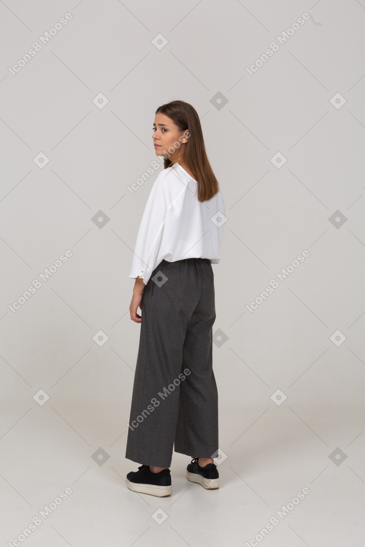 Three-quarter back view of a sad young lady in office clothing looking aside