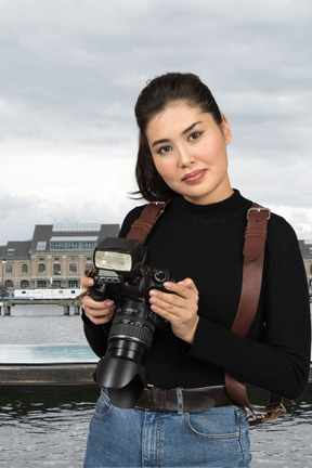 A woman holding a camera in front of a body of water