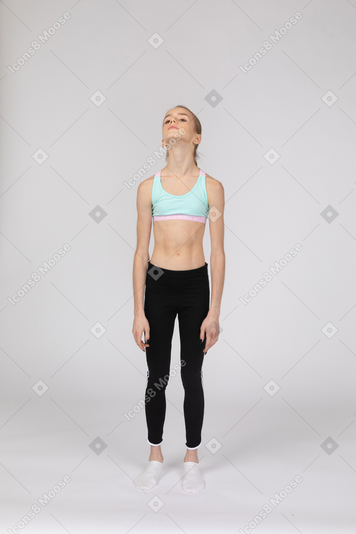 Vista frontal de una jovencita en ropa deportiva echando la cabeza hacia atrás mientras mira a la cámara
