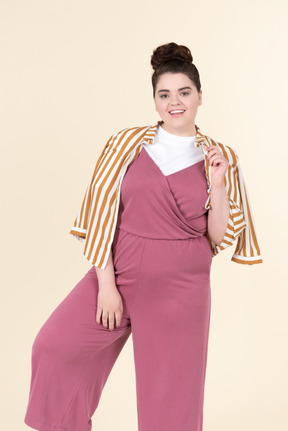 Young plus size woman in a pink jumpsuit and a striped jacket, posing against a pastel yellow background