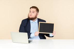 Serious looking young overweight office worker holding small blackboard