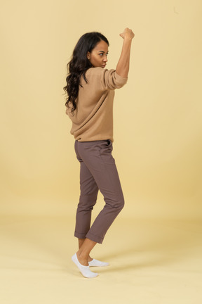 Side view of a strong dark-skinned young female raising hand while putting hand on hip