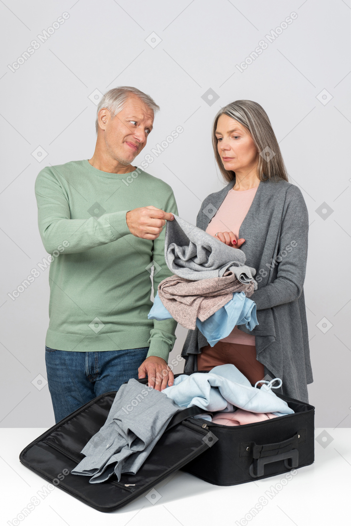 Middle aged couple holding clothes and preparing a suitcase
