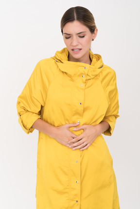 Frau in einem gelben mantel, der arme auf ihrem magen hält