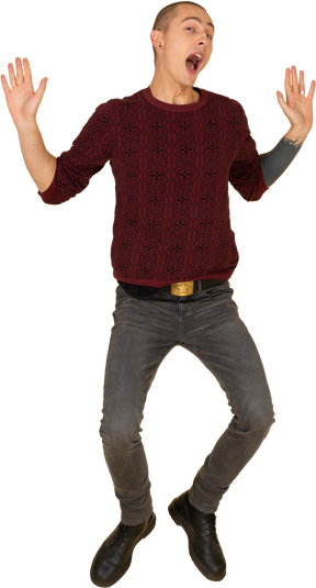 Front view of a jumping young man in red pullover raising his hands