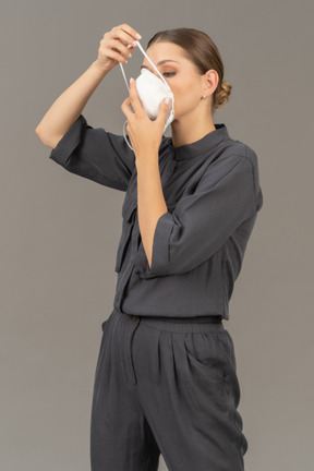 Woman in gray coveralls putting on a respirator