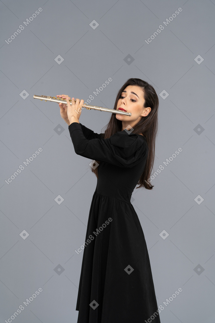 Vista de três quartos de uma jovem séria de vestido preto tocando flauta