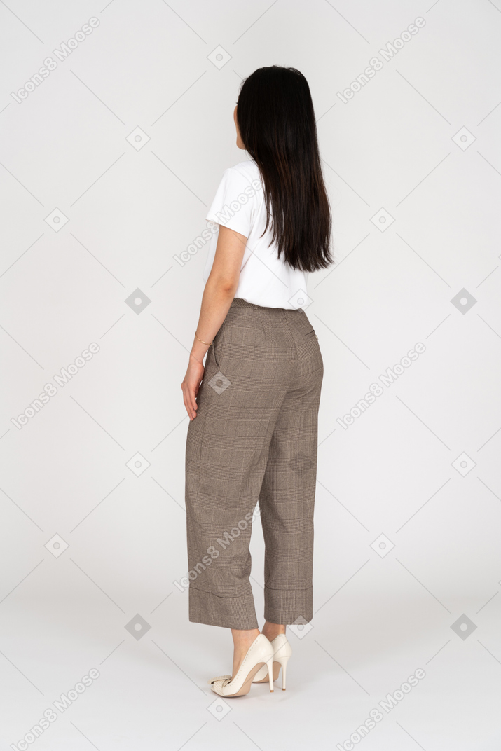 Vista posteriore di tre quarti di una giovane donna in calzoni e maglietta che si toccano il petto