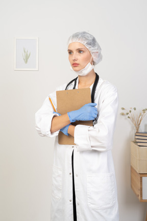 Vista de tres cuartos de una joven doctora sosteniendo un lápiz y una tableta