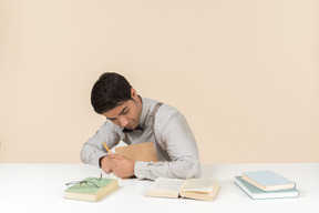 Young adult student sitting at the table and writing something down in the book