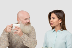 Bearded elderly man with mug and puzzled woman looking at him
