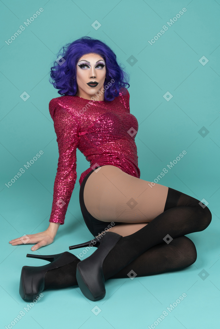 Portrait of a drag queen in pink sequin dress sitting on the ground & leaning back