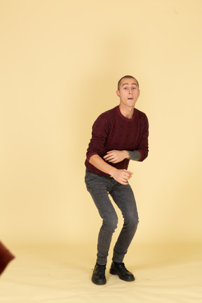 Front view of a surprised young man in red pullover ready to jump