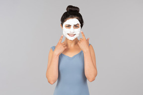 Woman with white facial mask on pointing at her face