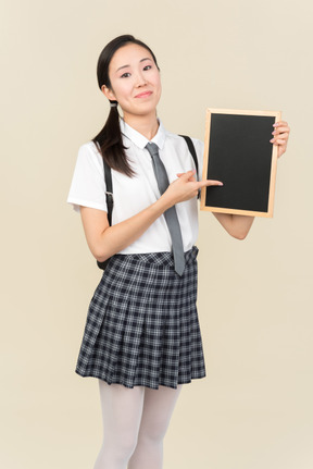 Smiling asian school girl pointing at small black board