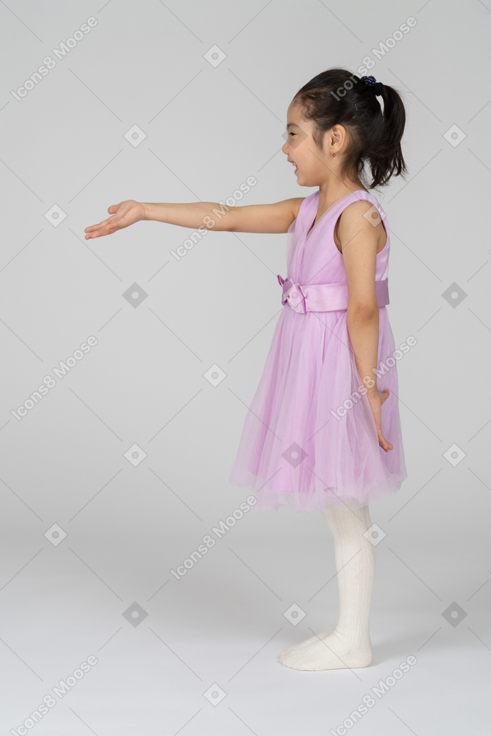 Vista lateral de uma menina em um vestido bonito, estendendo o braço direito