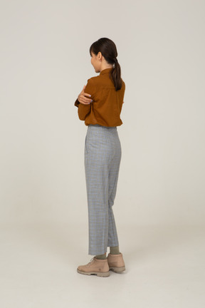 Vista posteriore di tre quarti di una giovane donna asiatica offesa in calzoni e camicetta che incrocia le braccia