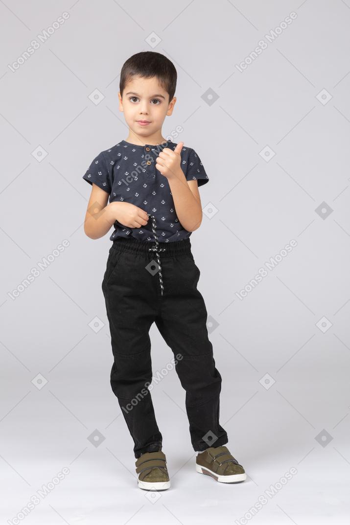 Вид спереди мальчика в повседневной одежде, смотрящего в камеру и показывающего большой палец вверх